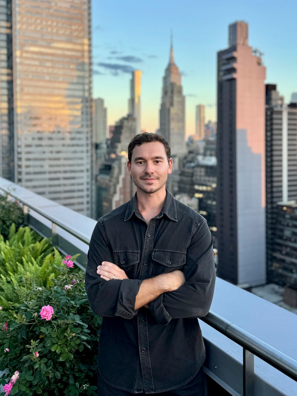 Alex Jastrzab on a rooftop terrace, the Manhattan skyline behind him at dusk.